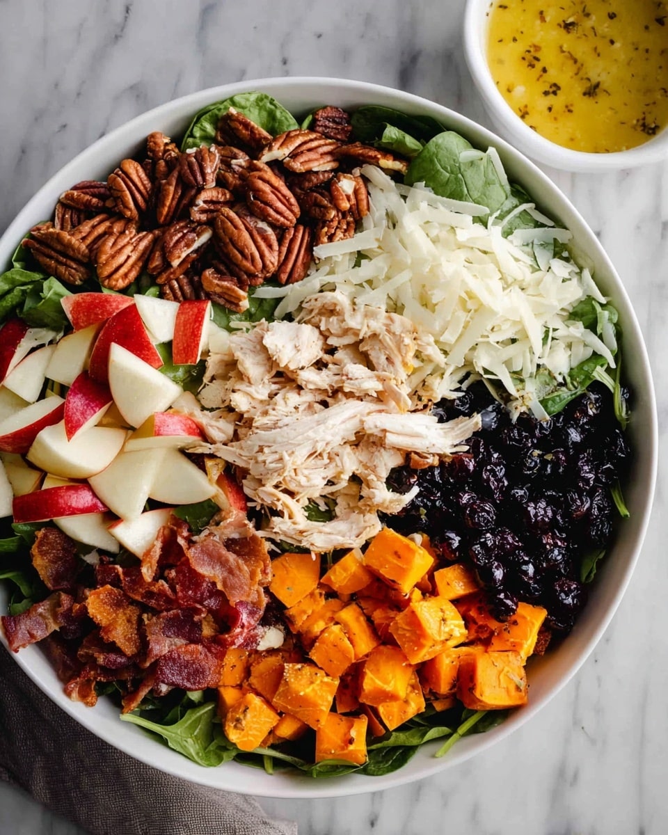 A white bowl filled with a colorful layered salad, starting with a base of green leafy spinach. On top, there are six distinct sections: small brown pecans on the top left, white shaved cheese just below them, diced red apple pieces with white flesh next to the pecans, crispy brown bacon strips running horizontally in the middle, shredded white chicken right beneath the bacon, dark dried blueberries arranged beside the chicken, and bright orange roasted sweet potato cubes at the bottom right. A small white bowl with a yellow dressing with visible seasoning sits nearby on a white marbled surface. Photo taken with an iphone --ar 4:5 --v 7