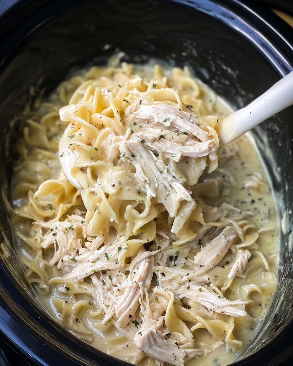 The dish shows a single layer of twisted, pale yellow noodles mixed with shredded pieces of white cooked chicken. The noodles have a slightly shiny texture, coated in a light broth or sauce that makes them glisten. Small bits of green herbs are scattered throughout the dish, adding subtle specks of color among the noodles and chicken. The food is served on a simple white plate placed on a white marbled surface. Photo taken with an iphone --ar 4:5 --v 7