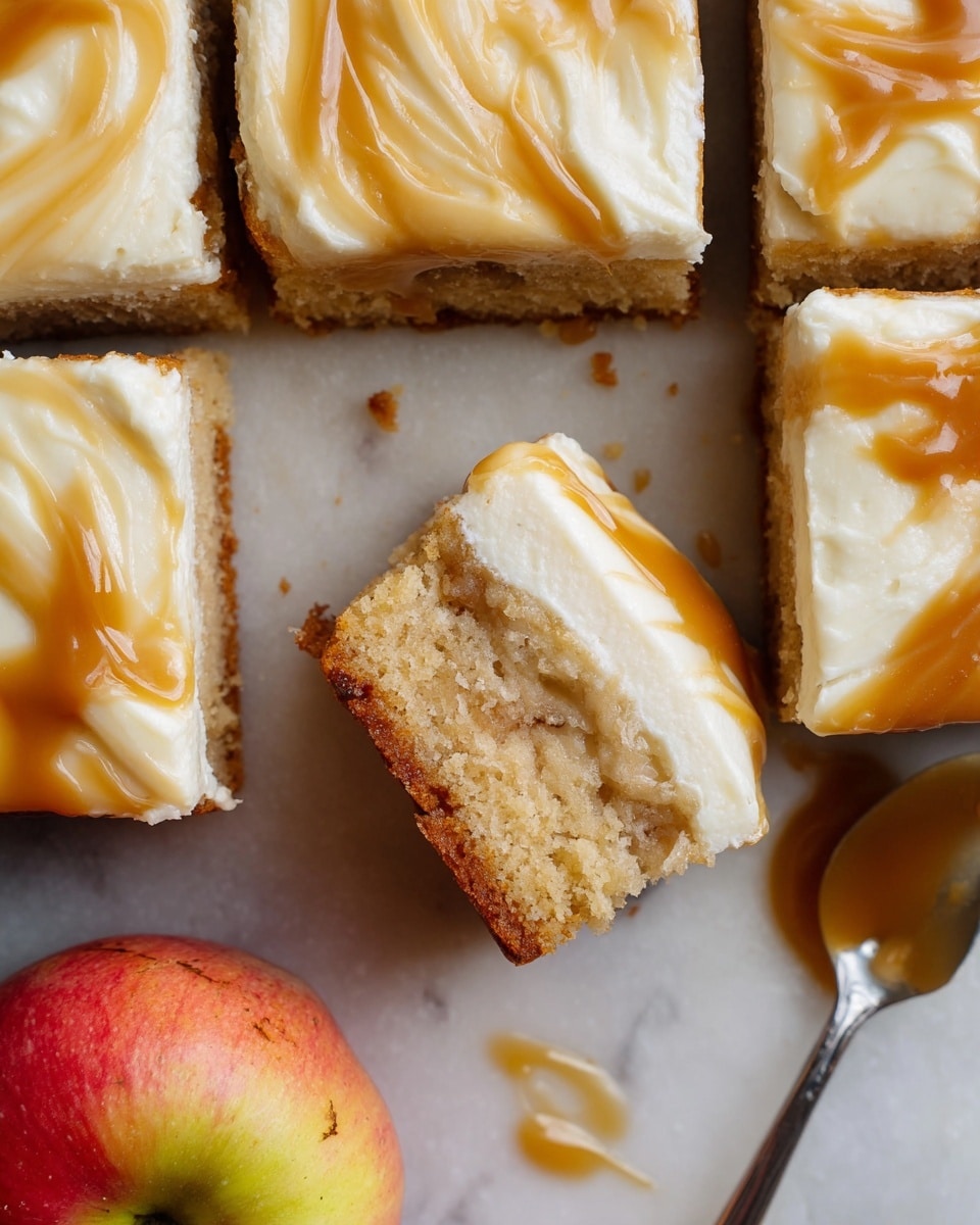 The image shows a tray of square apple cake pieces, cut into twelve even squares arranged in a 3x4 grid. Each piece has two visible layers: a thick, moist, light brown cake base with a slightly crumbly texture, and a creamy white frosting layer on top. The frosting is smooth and swirled with glossy caramel sauce, giving a marbled effect with rich shades of amber and gold. One piece is slightly pulled out from the tray, showing the thickness and texture of the cake and frosting. The cake rests on brown parchment paper, with two red apples partially visible in the background, all placed on a white marbled surface. A spoon with caramel sauce is on the left side, and a piece of beige linen cloth is in the left corner. Photo taken with an iphone --ar 4:5 --v 7