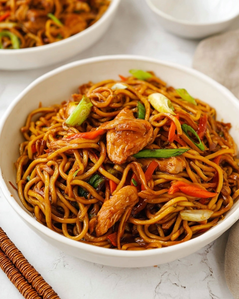 A white bowl filled with two main layers: the bottom layer is long, thick noodles with a shiny brown sauce, mixed with small pieces of bright orange carrot and green scallion slices, and the top layer has several pieces of browned, cooked chicken among the noodles. The colors include glossy brown from the sauce, golden brown from the chicken, and pops of orange and green from the vegetables. The bowl sits on a white marbled surface, with part of another white bowl partially visible in the background. A pair of chopsticks wrapped in brown is placed nearby. Photo taken with an iphone --ar 4:5 --v 7