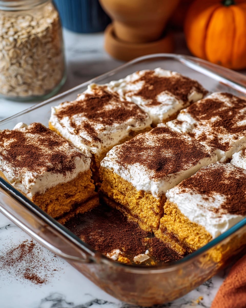 The image shows a baked pumpkin dessert cut into six square pieces inside a clear glass baking dish with blue handles placed on a white marbled surface. Each piece has two main visible layers: a thick, dense, orange pumpkin cake base and a fluffy, white cream layer on top, unevenly spread with swirls of a darker brown spice, likely cinnamon, dusted generously across the cream. The dessert looks moist and soft, with the brown spice giving a textured look to the creamy layer. The middle piece is removed, revealing the sponge-like texture of the cake layer and some moist crumbs left at the bottom. Photo taken with an iphone --ar 4:5 --v 7