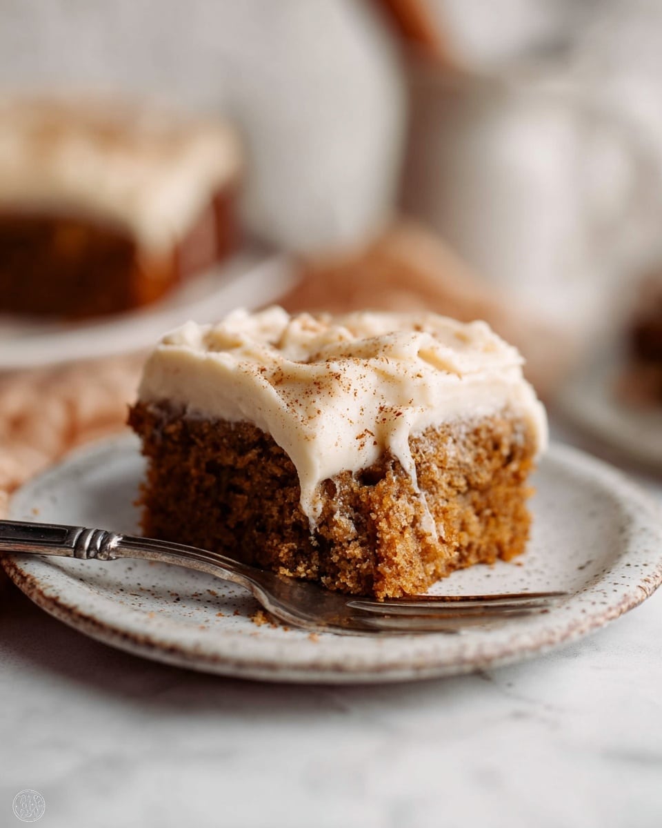 A square slice of moist, brown cake with a soft, crumbly texture sits on a white plate with a speckled edge. It is topped with a thick, creamy layer of off-white frosting sprinkled lightly with a bit of cinnamon or spice on top. A silver fork presses into the frosting near the front, cutting through the frosting and cake, showing the contrast between the smooth frosting and textured cake. The scene is set on a white marbled surface with a blurred background, giving a cozy and inviting feel. Photo taken with an iphone --ar 4:5 --v 7