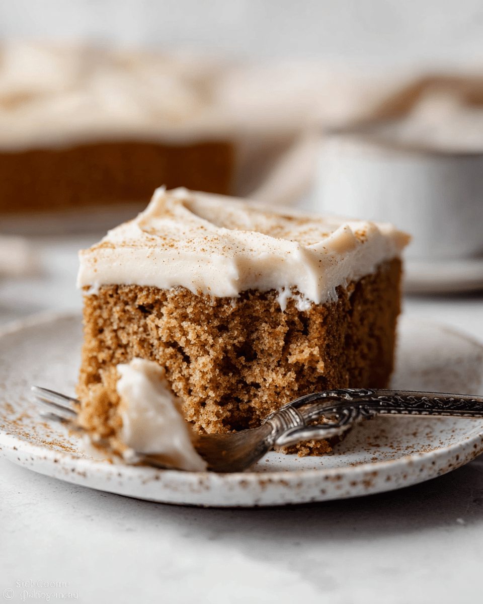 The image shows a close-up view of squares of cake with two distinct layers: the bottom layer is a thick, moist, brown spongy cake with a crumbly texture, and the top layer is a creamy, smooth, off-white frosting that is evenly spread and sprinkled lightly with a fine dusting of cinnamon or spice powder. The cake pieces are set close together on a white marbled textured surface with some crumbs scattered around the cut edges. Photo taken with an iphone --ar 4:5 --v 7