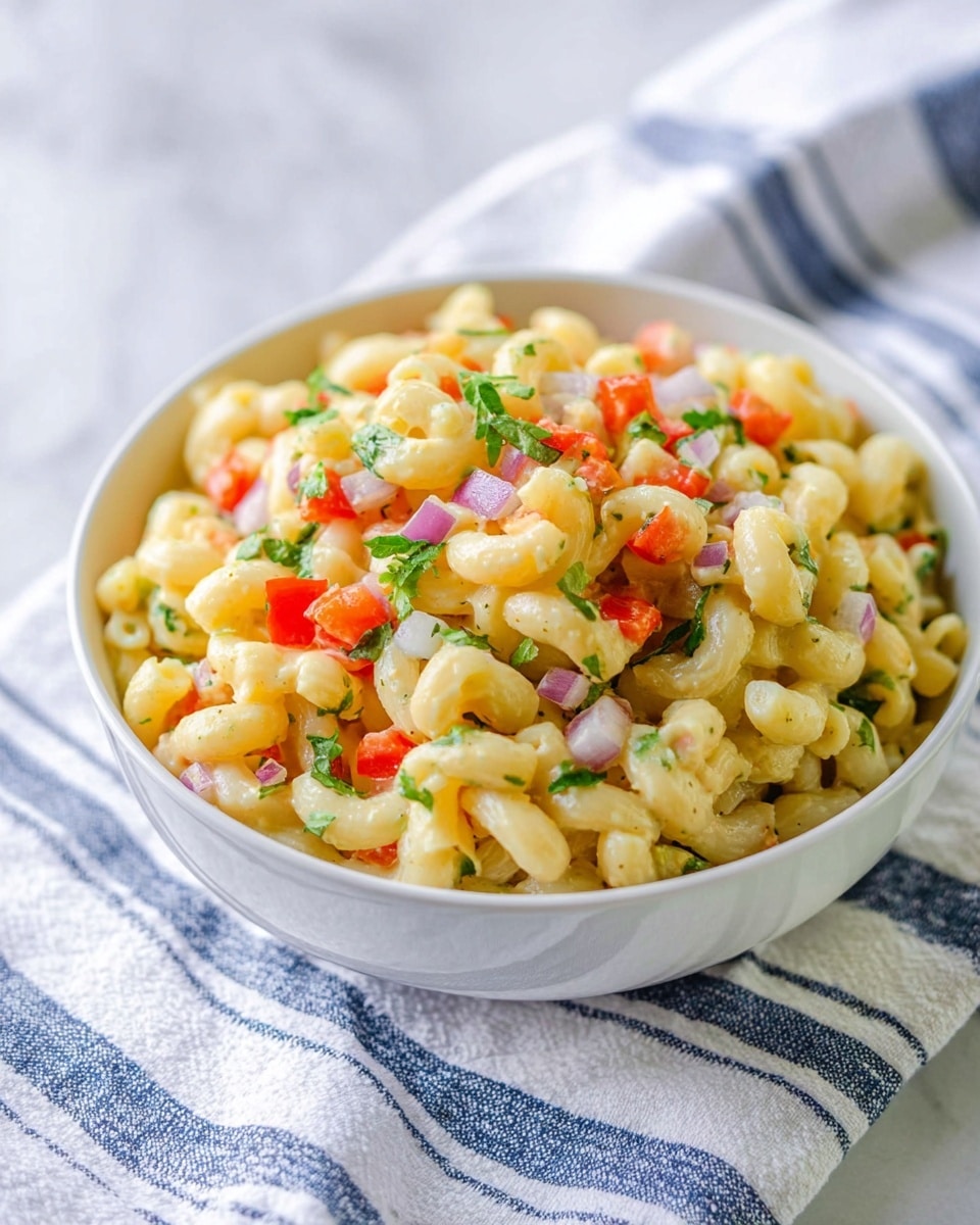 A white bowl filled with three visible layers of food: the bottom layer is a creamy light yellow pasta made of elbow macaroni; the middle layer has small chopped pieces of light purple onion and green herbs; the top layer includes diced bright red bell peppers and small green parsley leaves mixed with the pasta. The bowl sits on a white marbled surface with a white cloth that has blue stripes beneath it. The overall look is fresh and colorful, with a soft texture. photo taken with an iphone --ar 4:5 --v 7