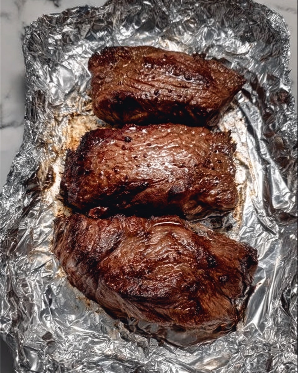 Three pieces of well-cooked, dark brown grilled meat rest on a sheet of silver foil. The meat has a slightly crispy outer layer with visible grill marks and a textured, juicy surface. Each piece is thick and irregularly shaped, showing some charred edges. The background is a white marbled texture. photo taken with an iphone --ar 4:5 --v 7