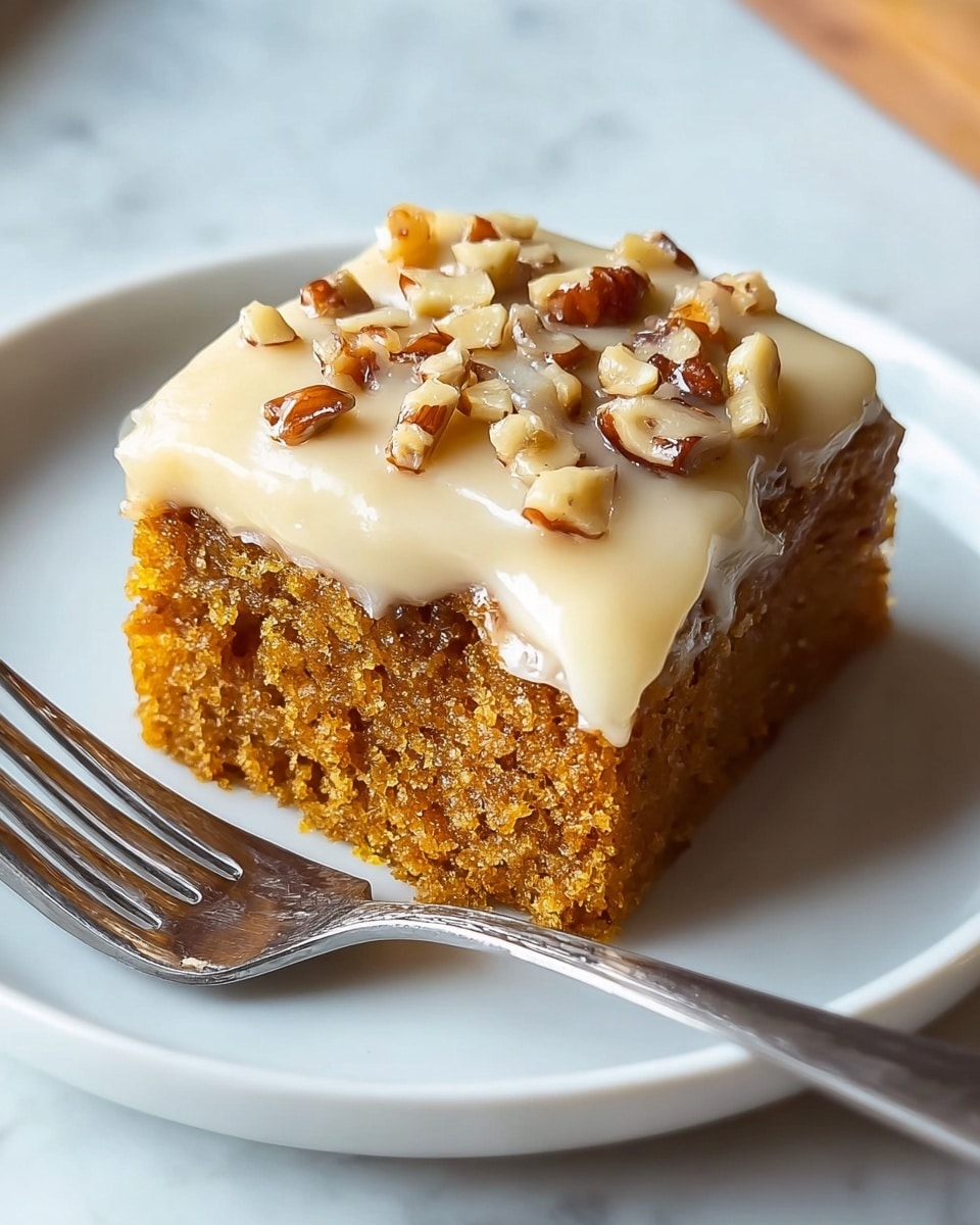 A single square piece of moist brown cake sits on a white plate, topped with a thick layer of creamy, light beige frosting that slightly melts over the edges. Small pieces of chopped nuts in shades of light tan and dark brown are sprinkled on top of the frosting. A silver fork lies next to the cake on the plate, all placed on a white marbled surface. photo taken with an iphone --ar 4:5 --v 7