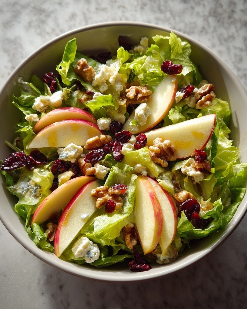 A white bowl filled with a fresh salad shows a base layer of green leafy lettuce with some purple leaves mixed in. On top, there are light yellow chunks and thin slices of red apple pieces spread evenly. White crumbled cheese is sprinkled throughout the salad, followed by a generous layer of glossy brown whole walnuts. Small dark red dried cranberries are scattered across the salad, adding color contrast. The ingredients look fresh and slightly shiny with dressing. The whole scene sits on a white marbled surface. photo taken with an iphone --ar 4:5 --v 7