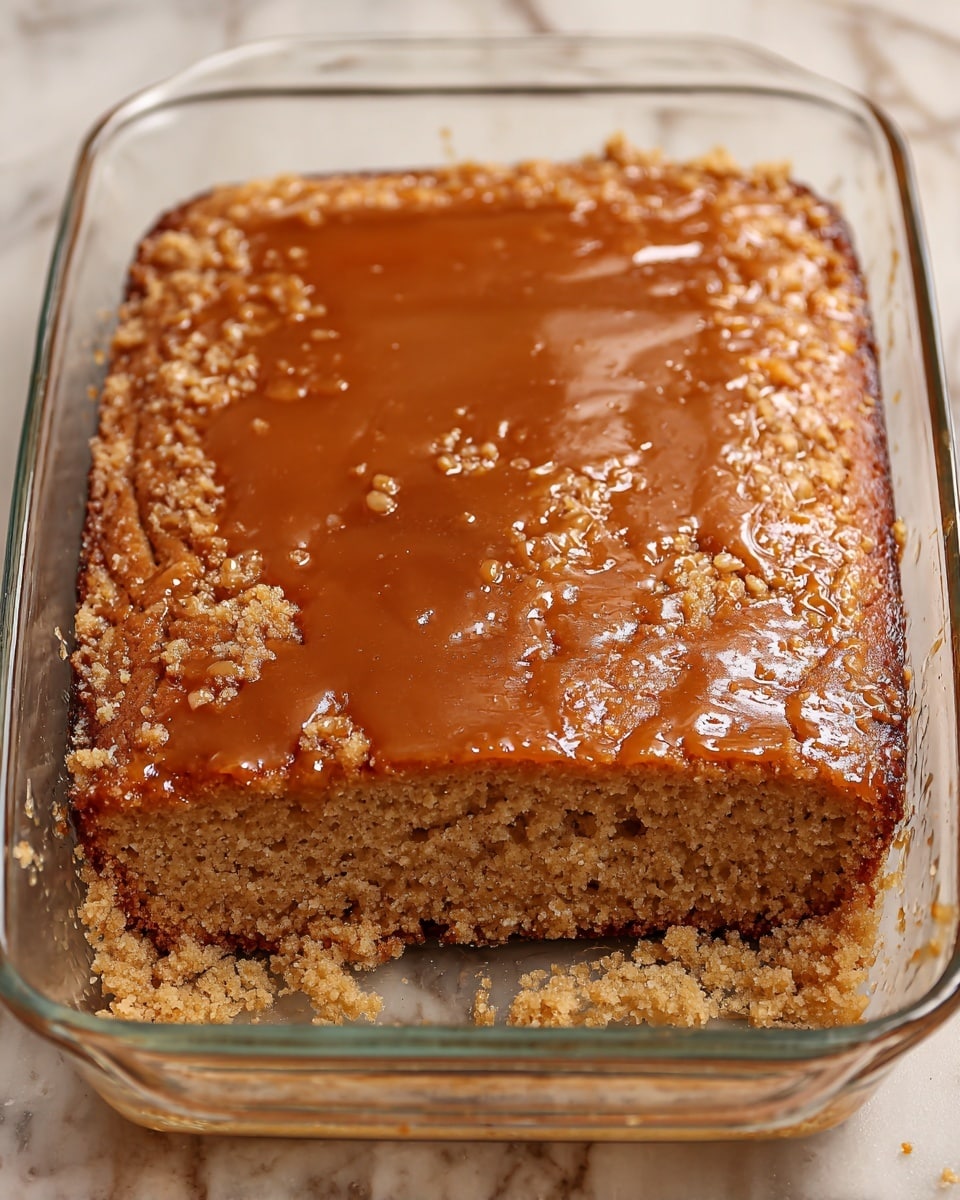A square piece of moist, light brown cake sits centered on a white plate with a white marbled texture beneath it. The cake has a dense, crumbly texture with visible small air pockets and is topped with a shiny, slightly darker caramel glaze that drips down the sides. On top of the glaze, there is a round scoop of creamy white ice cream, melting slightly and creating streaks that run down the front of the cake, mixing with the caramel sauce pooled on the plate. photo taken with an iphone --ar 4:5 --v 7