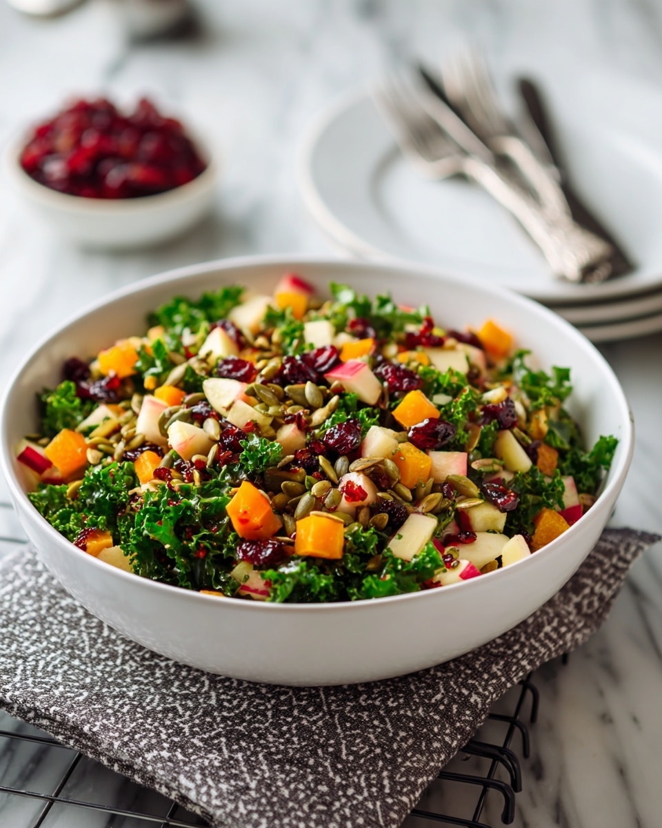 A large white bowl filled with a colorful salad sits on a metal wire rack over a white marbled surface. The salad has multiple layers, starting with dark green curly kale leaves as the base, mixed with small cubes of bright orange butternut squash, pale beige apple pieces with red skin, and deep red dried cranberries. Scattered on top are light green pumpkin seeds and small brown grains, adding texture. The bowl is placed near two white plates and silverware in the background, softly blurred. The lighting highlights the fresh, varied colors of the salad. photo taken with an iphone --ar 4:5 --v 7