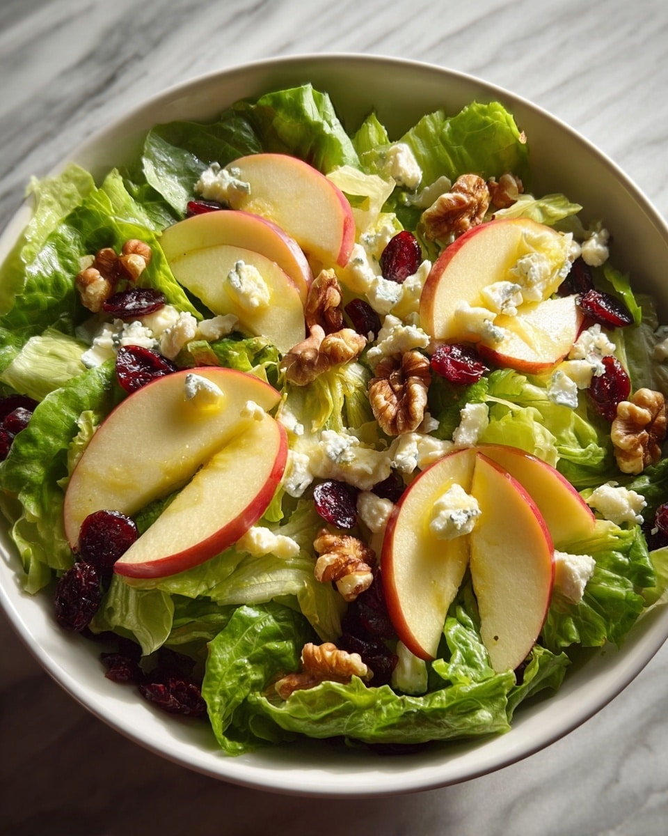 A fresh salad is shown in a white bowl set on a white marbled texture surface. The bottom layer is bright green leafy lettuce with a fresh, slightly wrinkled texture. On top of the lettuce, thinly sliced pale yellow apple slices with pinkish-red edges are evenly arranged around the bowl. Scattered between the apples are small clusters of white, crumbly cheese. Dark red dried cranberries add a touch of deep color contrasted with the light ingredients. Light and glossy brown walnut pieces are evenly spread across the salad, adding texture and richness. The salad looks fresh and colorful with a balanced mix of crisp, soft, and crunchy textures. Photo taken with an iphone --ar 4:5 --v 7