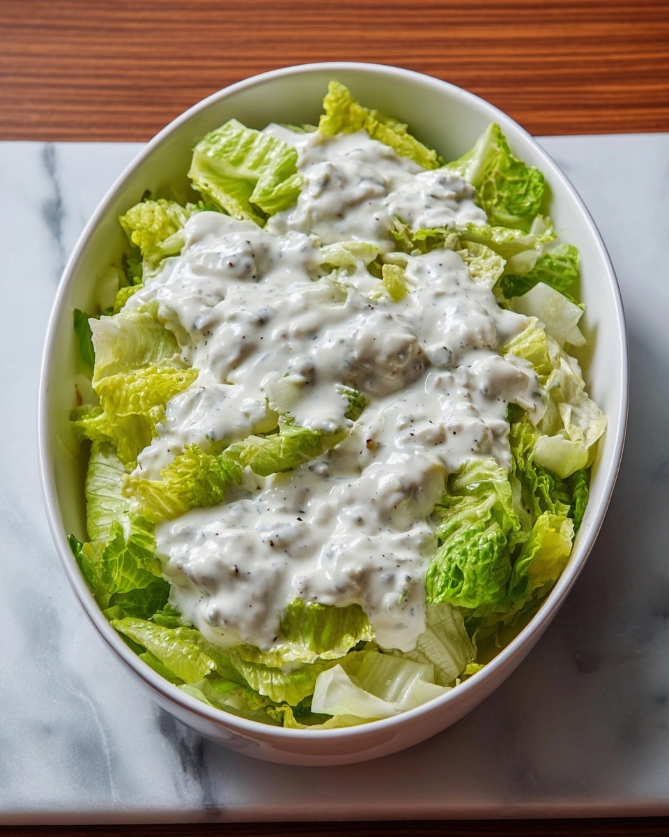 A white bowl filled with creamy salad mostly made of light green and pale yellow lettuce leaves, coated in a smooth, white dressing, with a fork lifting a bite of the salad showing a mix of crisp, slightly curled leaves and dressing. The bowl sits on a white marbled surface with a striped cloth underneath, and a white dish filled with more salad is blurred in the background. photo taken with an iphone --ar 4:5 --v 7