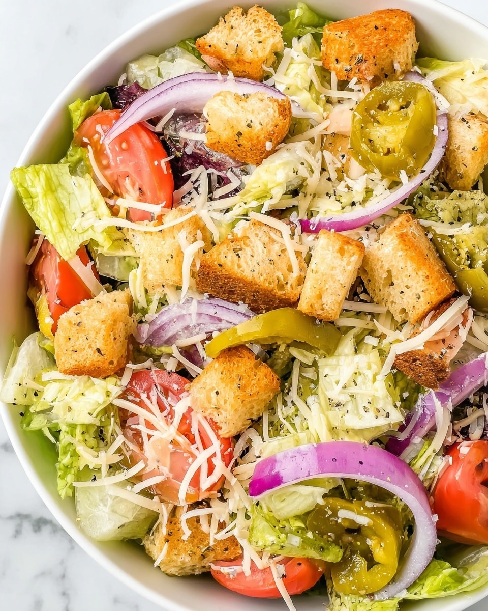 A fresh salad in a white scalloped bowl on a white marbled surface, with a black fork in it; the salad has several layers starting with a base of light green chopped lettuce, topped with slices of bright red tomato and pale green pepperoncini peppers. Scattered black olives and thin rings of purple onion add color contrast, while small golden brown croutons and a sprinkle of white shredded cheese cover the top. In the background on the right side, there is a light wooden board with extra shredded cheese, and partially visible golden bread rolls on the edge of the frame. photo taken with an iphone --ar 4:5 --v 7