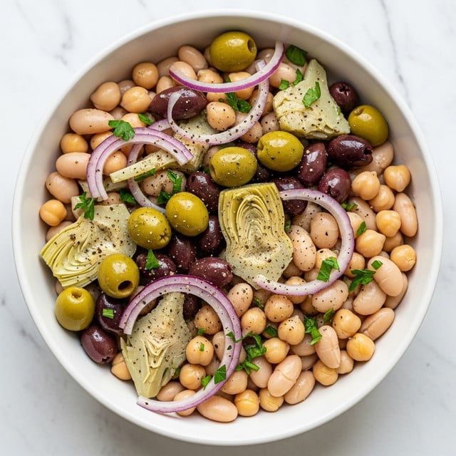 A white bowl filled with a colorful bean salad showing three main layers: the base layer has smooth, round white beans mixed with smaller beige chickpeas; the middle layer includes bright green olives and light green artichoke hearts cut into halves and quarters; the top layer is thin slices of purple-red onion and finely chopped green herbs scattered throughout, all glistening with olive oil and seasoned with black pepper, on a white marbled background. photo taken with an iphone --ar 4:5 --v 7
