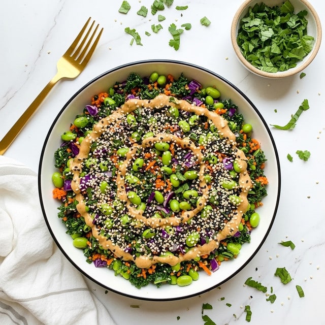 A white bowl with a dark rim is filled with a colorful salad made of many small chopped pieces. The bottom layer is a mix of green vegetables like chopped kale and edamame beans, mixed with some orange bits that look like shredded carrots and small chunks of purple cabbage. On top, there are sesame seeds sprinkled all over, giving a textured look with white and black specks. A creamy, light brown dressing is drizzled unevenly across the salad. Around the bowl, there are scattered bits of chopped green herbs on a white marbled surface, with a small beige bowl filled with fresh chopped green herbs nearby. A gold fork lies to the upper left and part of a white cloth with light stripes is visible on the lower left side. Photo taken with an iphone --ar 4:5 --v 7