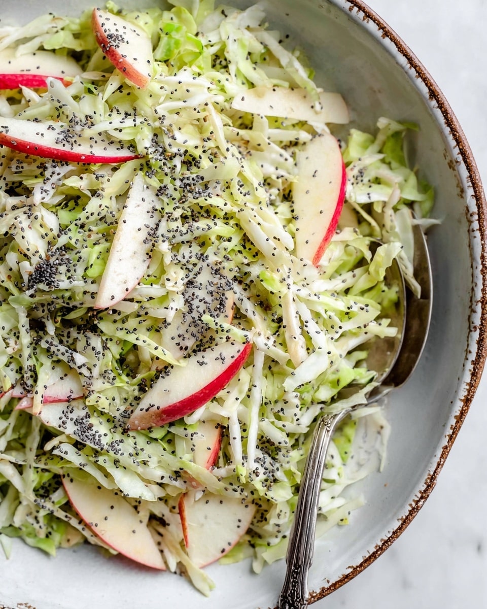 A large white bowl filled with a fresh salad showing about three layers: a base of thinly sliced light green Brussels sprouts, mixed with long thin strips of pale yellow and white apple with red edges, and sprinkled with small round black poppy seeds evenly across the top. The textures include the crisp, shredded Brussels sprouts and the smooth, slightly translucent apple slices. A vintage silver fork rests inside the bowl, partially buried in the salad. The bowl sits on a white marbled surface with scattered poppy seeds nearby and a small white bowl filled with more poppy seeds just beside it. Photo taken with an iphone --ar 4:5 --v 7