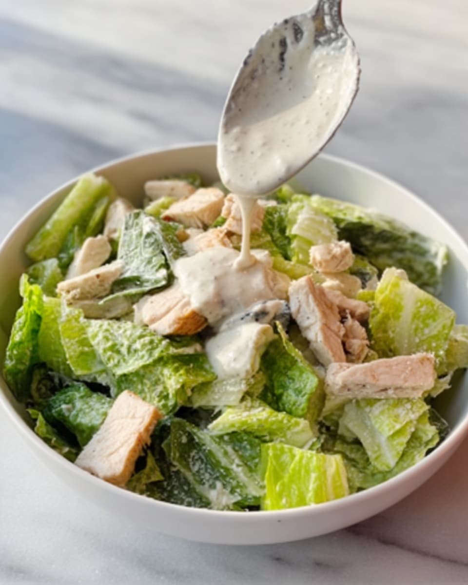 The image shows a white plate with a blue rim holding a simple Caesar salad. The dish has a base layer of fresh light green lettuce leaves, chopped into medium pieces. On top, there are several golden brown grilled chicken strips scattered evenly. Light creamy white Caesar dressing is drizzled over the chicken and lettuce, adding a smooth texture. A silver fork lies on the left side of the plate. The background is a white marbled surface with part of a cup of light brown coffee and a white cloth with red stripes visible near the top edge. photo taken with an iphone --ar 4:5 --v 7
