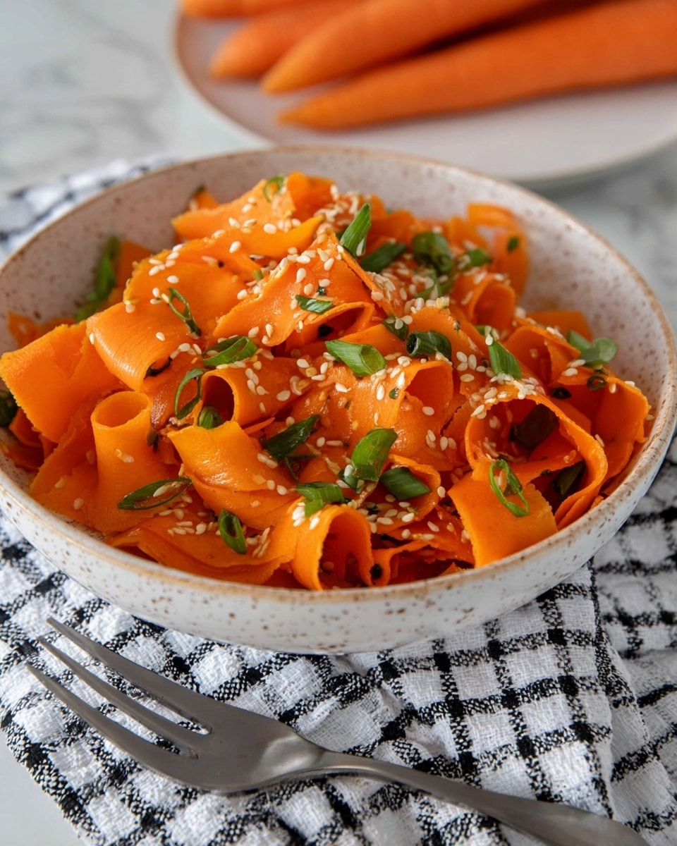 A round white bowl filled with thin, wide ribbons of bright orange carrot slices, loosely piled in several overlapping layers. Scattered across the carrot ribbons are small white sesame seeds and chopped green onion pieces, adding specks of white and green color. The bowl is placed on a white marbled surface, with a few whole carrots lying beside it, and a fork on a checkered cloth nearby. photo taken with an iphone --ar 4:5 --v 7