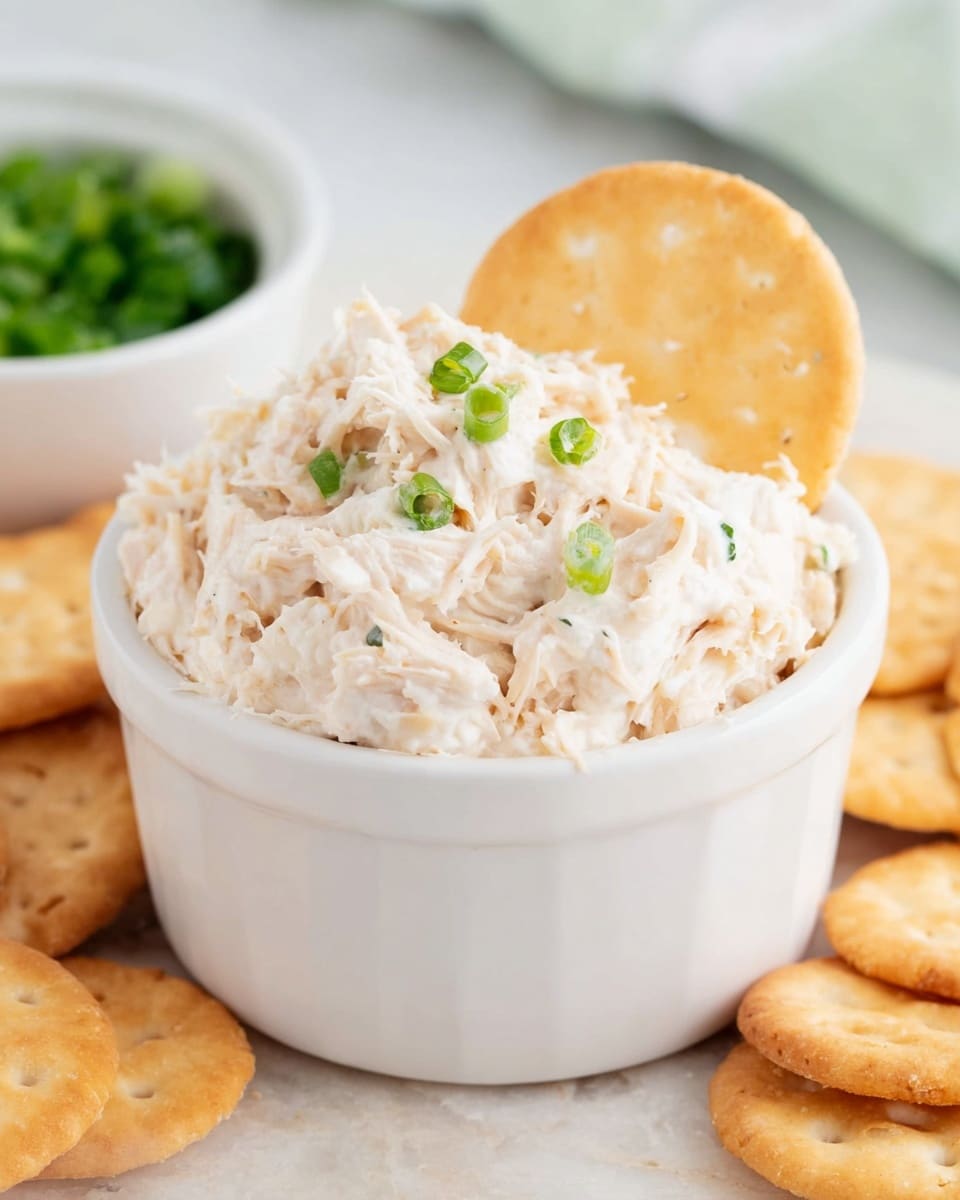 A clear glass bowl sits on a white marbled surface, filled with a thick, creamy mixture that is mostly white with some light orange shreds and small bits of green scattered throughout. The mixture has a soft, slightly chunky texture and looks like a blend of shredded ingredients. A yellow silicone spatula with a wooden handle is partially inserted into the mixture, resting on the right side of the bowl. The scene is bright and clean, focusing closely on the textured mixture inside the bowl. photo taken with an iphone --ar 4:5 --v 7