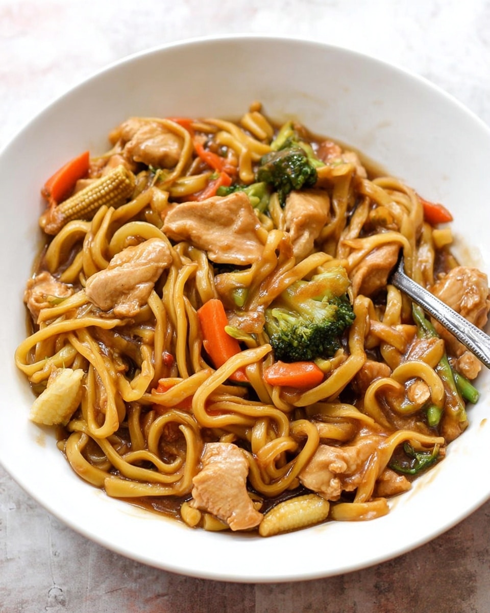 A white bowl filled with a noodle stir-fry showing around three layers: the bottom layer is glossy brown sauce coating thick yellow noodles that twist around the bowl; the middle layer features bite-sized pieces of light brown chicken along with chunks of bright orange carrot strips and small green broccoli florets; the top layer is scattered with pale yellow baby corn pieces and additional sauce covering some ingredients, all resting on a white marbled surface with a metal fork partially inside the bowl photo taken with an iphone --ar 4:5 --v 7