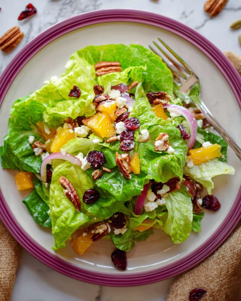 A fresh salad sits on a white plate with a purple rim, placed on a white marbled surface. The salad has several layers starting with large green lettuce leaves forming the base; scattered on top are bright small orange and yellow bell pepper pieces, thin slices of purple onion, and chunks of white cheese. Mixed throughout are whole pecans and dark red dried cranberries, adding textured color. A silver fork rests on top of the salad near the upper edge of the plate. Some seeds and dried cranberries are scattered around the plate on the white marbled surface. Photo taken with an iphone --ar 4:5 --v 7