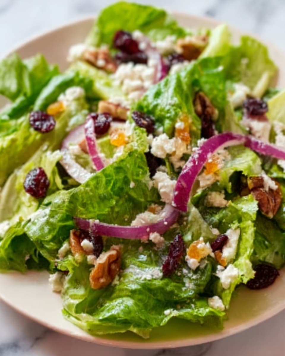 A fresh salad is shown on a white plate sitting on a white marbled surface. The base layer is bright green leafy lettuce with visible veins and a slightly crisp texture. Scattered on top are thinly sliced red onions, dark red dried cranberries, and small beige pieces of crumbled cheese. There are also small, rough textured brown nuts sprinkled around, adding depth and crunch. The colors contrast well, with the green leaves, purple onions, red cranberries, white cheese, and brown nuts making the salad look vibrant and fresh. Photo taken with an iphone --ar 4:5 --v 7