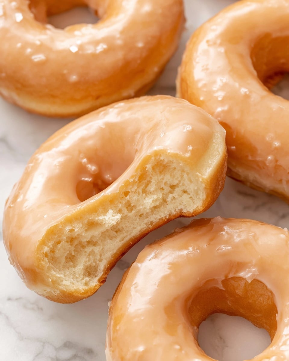 A white bowl is filled with several small, round doughnut holes coated in a light shiny glaze. Surrounding the bowl on a white marbled surface are larger, round glazed doughnuts with a smooth, glossy orange-brown finish. The doughnut holes and doughnuts have a soft, slightly uneven texture under the glaze that catches the light, showing a golden color beneath. The bowl sits centrally with doughnuts spaced casually around it, creating a warm and inviting look. photo taken with an iphone --ar 4:5 --v 7