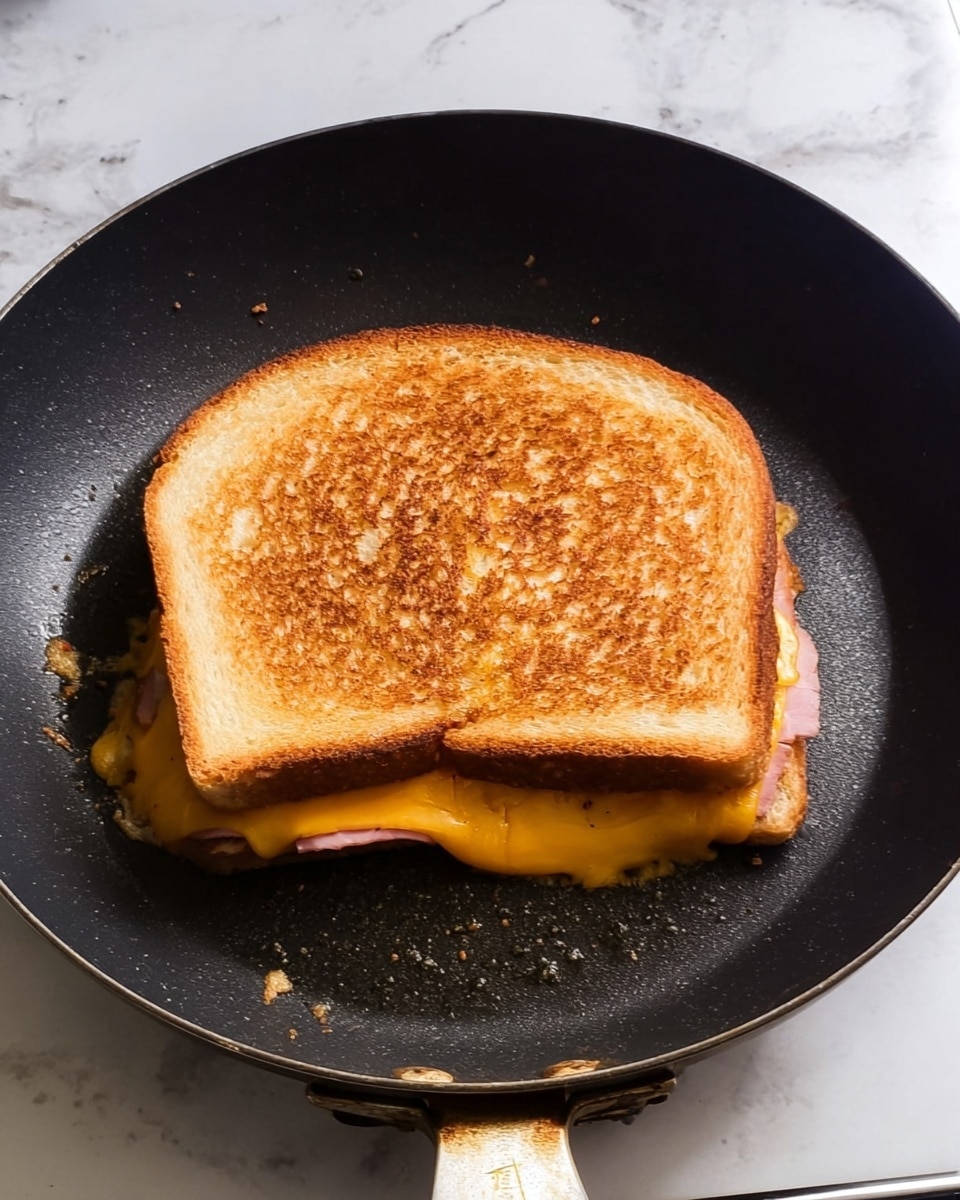 A toasted sandwich cut diagonally into two triangles sits on a white plate placed on a white marbled surface. Each sandwich half shows two layers of golden brown toasted bread with a crispy texture outside, enclosing a thick layer of pink ham and melted orange cheddar cheese that slightly oozes out at the edges. The sandwich halves are stacked slightly overlapping, showing the layers clearly. photo taken with an iphone --ar 4:5 --v 7