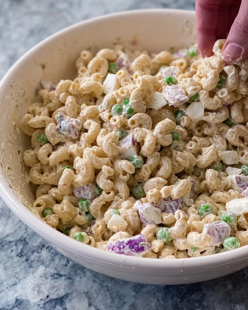 The image shows a close-up view of a creamy macaroni salad in a white bowl. The salad has about two layers mixed together: the main layer is short, tubular elbow macaroni coated in a beige creamy dressing, giving it a smooth and slightly shiny texture. Scattered throughout are small bits of green peas and purple onion pieces, adding a slight contrast in color. There are also chunks of white boiled eggs spread evenly in the mix. The bowl is set on a white marbled surface, and a woman's hand is reaching into the salad from the top right corner. photo taken with an iphone --ar 4:5 --v 7