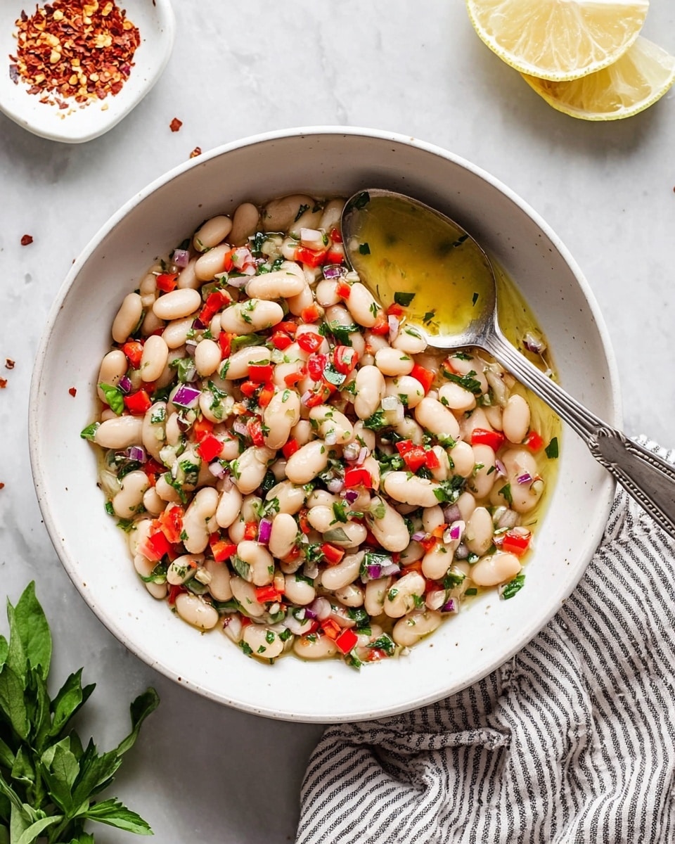 In a clear glass bowl on a white marbled surface, there is a colorful mix of ingredients arranged in layers. The bottom layer consists of white beans, covering about half the bowl with some beans scattered on the sides. On the lower right side, finely chopped red bell peppers create a bright red patch. To the left of the peppers, there's a small pile of finely chopped light purple shallots. Above these, a mound of shredded green herbs sits in the center, topped with a small amount of yellow lemon zest. Around the herbs are small piles of white salt, black pepper, and red chili flakes, along with finely minced garlic. A clear glass container is pouring golden olive oil over the right section of the beans. Nearby, two small white bowls hold extra pepper, salt, and chili flakes. Photo taken with an iphone --ar 4:5 --v 7