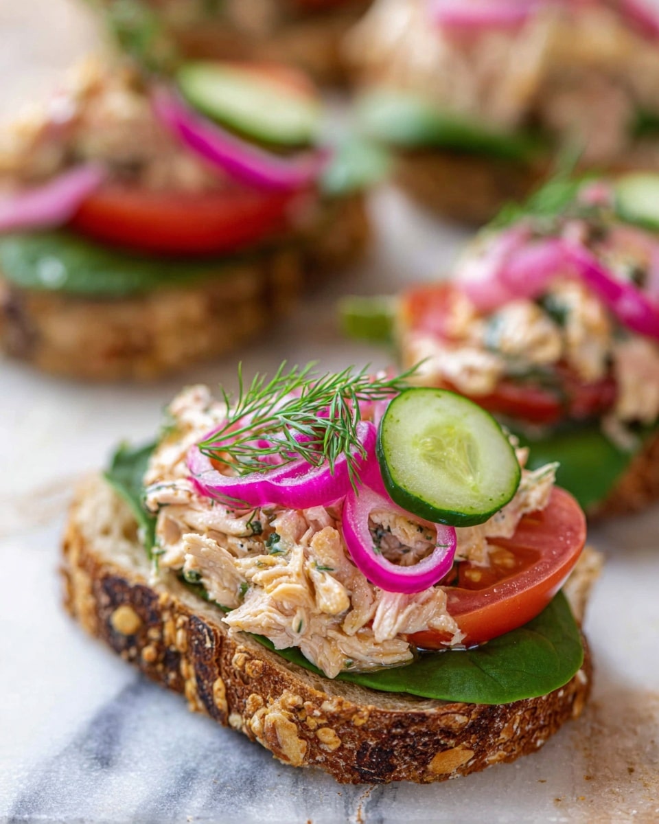 This image shows a sandwich open-faced on a white plate with a white marbled texture underneath. The bottom layer is a thick slice of toasted multigrain bread with visible seeds and grains that add texture and a golden-brown toasted edge. On top of this is a layer of mixed cooked chicken pieces that are light beige with some darker spots, giving a chunky and slightly moist look. Scattered on the chicken are thin slices of bright green cucumber and some vibrant purple-red rings of raw onion, adding a fresh and crunchy contrast. Small green herb sprigs are sprinkled lightly over the top, giving it a fresh, natural touch. Photo taken with an iphone --ar 4:5 --v 7
