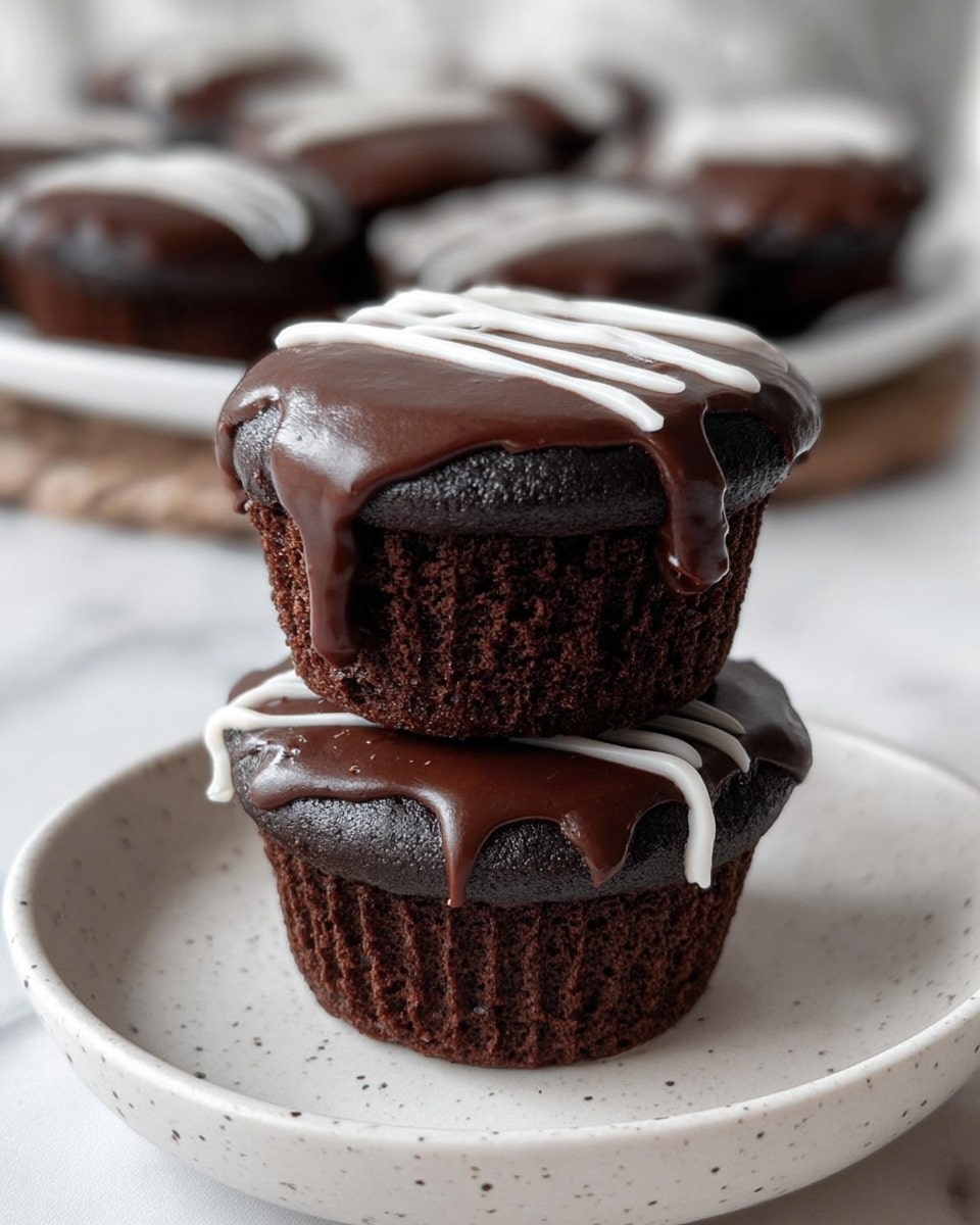 Two dark brown chocolate cupcakes are stacked on top of each other on a white plate with small speckles, set on a white marbled background. Each cupcake is topped with a smooth layer of glossy dark chocolate frosting that has a slightly uneven edge, and a thin white cream decoration is piped across the top of both, with some drip visible on the side of the bottom cupcake. In the background, several more cupcakes are arranged blurred on a white plate. Photo taken with an iphone --ar 4:5 --v 7