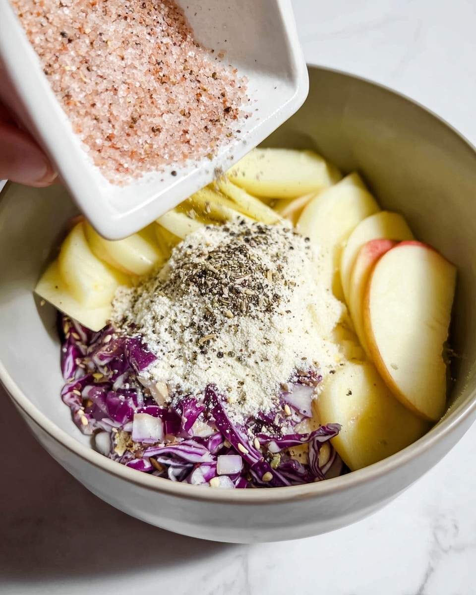 The image shows a close-up of a bowl with several layers of ingredients, including light yellow apple slices with smooth skin, small bits of chopped purple cabbage, a layer of white flour sprinkled unevenly over the vegetables, and some light brown seasoning. Above the bowl, a woman's hand is pouring a white rectangular dish holding two layers of seasonings: pink coarse salt on the bottom and black cracked pepper on top. The bowl is placed on a white marbled surface. photo taken with an iphone --ar 4:5 --v 7