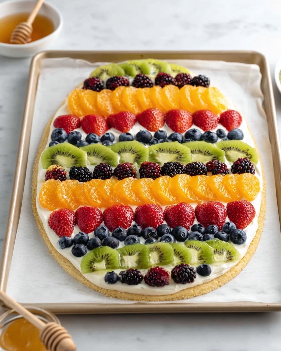A large, egg-shaped dessert lies on a baking tray lined with white paper, placed on a white marbled surface. The base is a light golden cookie crust topped with a thick layer of white cream. On top of the cream are neat rows of colorful fruits arranged in horizontal stripes: at the top and near the bottom are semi-circular slices of bright green kiwi; just below the top are segments of orange tangerine; large, red strawberries with glossy surfaces are placed below with small clusters of deep blue blueberries between them; tiny black blackberries create dense lines in the middle; alternating rows of kiwi, tangerines, strawberries, blueberries, and blackberries fill the entire shape with vibrant colors and textures. At the edge of the tray, there's a glimpse of a white bowl with honey and a wooden dipper. photo taken with an iphone --ar 4:5 --v 7