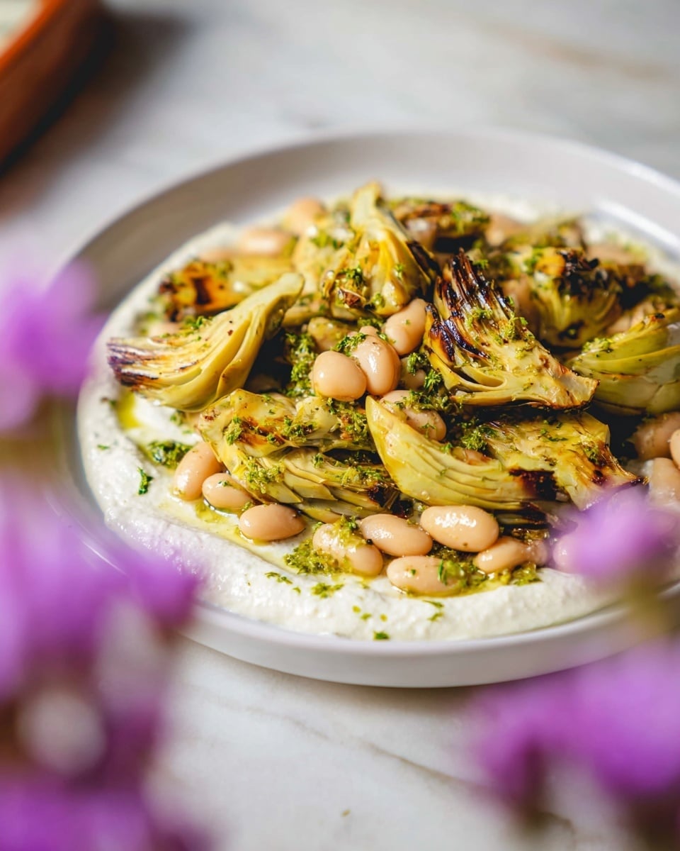 A white plate with a base layer of smooth, creamy white sauce spread evenly in a circular shape, topped with a second layer of grilled, golden yellow artichoke pieces that have dark brown char marks and a sprinkle of green herbs. Scattered among the artichokes are plump, light beige beans coated in a glistening herb dressing, adding texture and color contrast. The plate sits on a white marbled surface, with soft focus purple flowers blurred in the foreground. Photo taken with an iphone --ar 4:5 --v 7