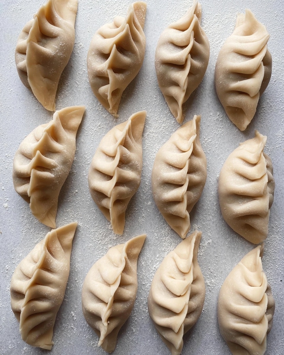 The image shows fifteen raw dumplings arranged in neat rows on a piece of light gray baking paper. Each dumpling is closely sealed with a wavy edge in the center, creating a folded pattern that looks soft and slightly thicker along the crease. The dough is pale beige with a smooth surface and a gentle matte finish. The dumplings are placed close together on a flat white marbled textured surface, with no other items visible in the frame. Photo taken with an iphone --ar 4:5 --v 7