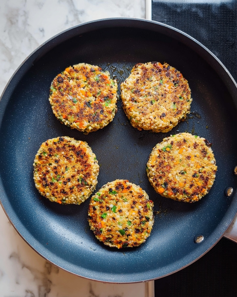 Five round lentil patties are cooking in a dark blue non-stick frying pan. Each patty is golden brown with small green herb pieces and darker lentils visible throughout. The patties are evenly spaced in a circular layout, with a slightly crispy texture on top showing light and dark brown spots from cooking. The pan sits on a black stovetop, and the background shows a white marbled texture. photo taken with an iphone --ar 4:5 --v 7