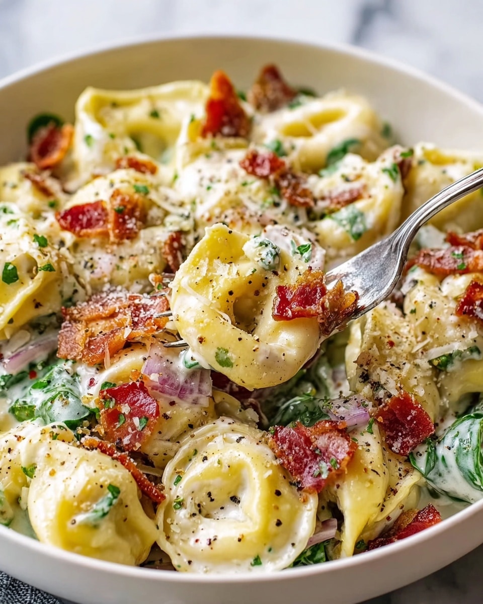 A white bowl filled with creamy tortellini pasta, each piece pale yellow and soft-looking, layered with crispy brown bacon pieces scattered throughout. Bright red cherry tomato halves are mixed in, adding pops of color, along with thin slices of light purple onion. The dish is sprinkled with finely chopped green herbs and black pepper, giving texture and contrast. The creamy sauce coats all the ingredients smoothly, creating a rich and inviting look. The bowl sits on a white marbled surface. photo taken with an iphone --ar 4:5 --v 7