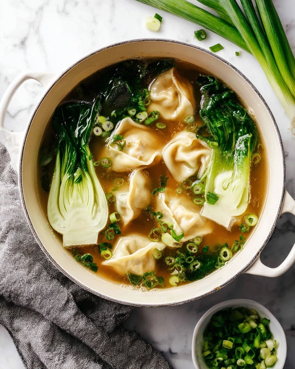 A white pot filled with light brown broth containing several pale beige dumplings with soft, folded edges floating on the surface. Three bright green bok choy halves with visible white stalks are placed inside the broth, contrasting with the dumplings. Small pieces of chopped dark green spring onions are sprinkled on top of the soup and floating in the broth. Next to the pot, a small white bowl holds more finely chopped bright green spring onions. The pot rests on a white marbled surface with a few whole green onions nearby and a grey cloth partially visible in the lower left corner. photo taken with an iphone --ar 4:5 --v 7