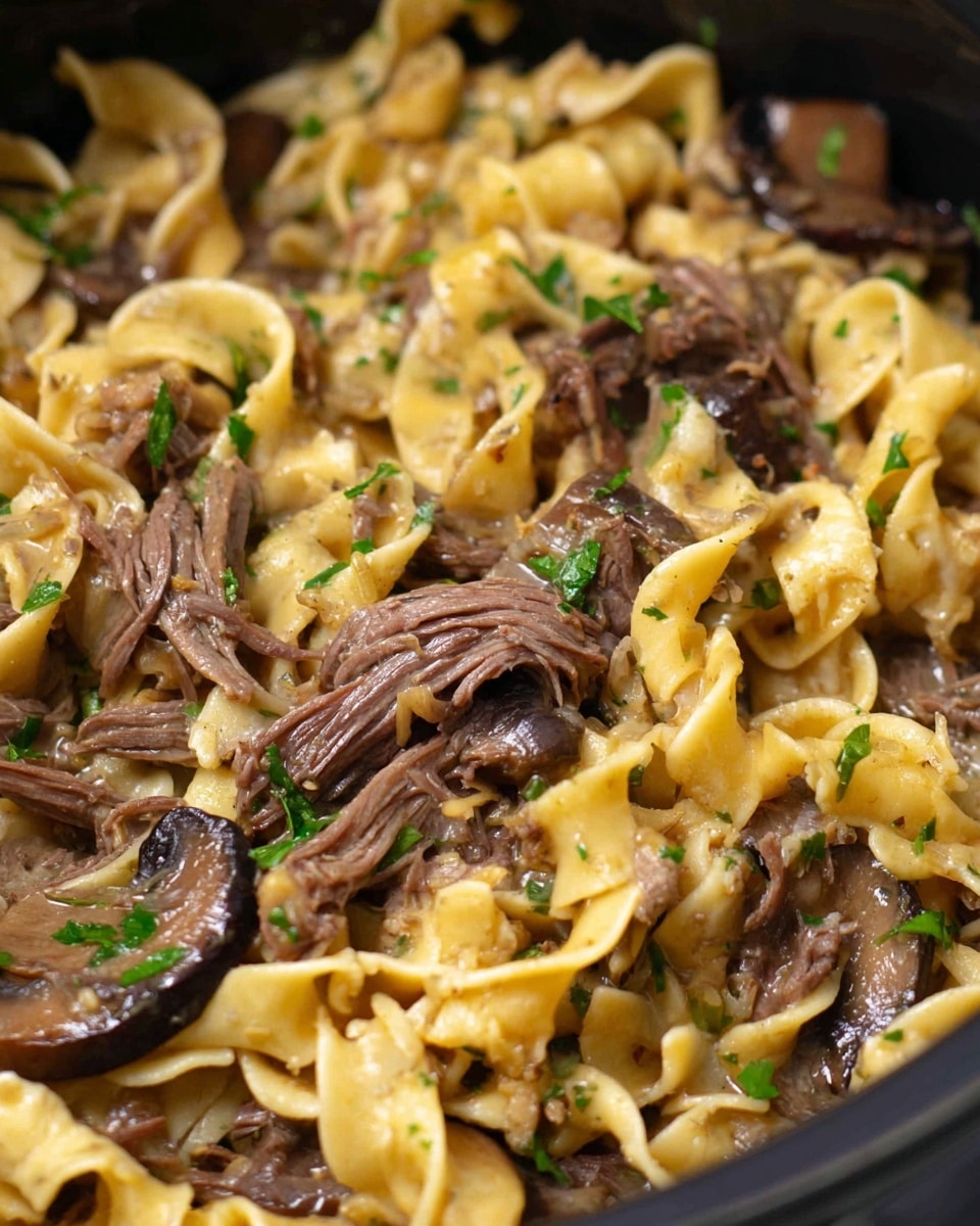 This close-up shows a dish in a black pot with wide, flat egg noodles in light yellow mixed with shredded beef in dark brown. There are slices of cooked mushrooms in dark brown with a slightly glossy finish, scattered throughout. Small bits of fresh green parsley tops the dish. The textures show tender meat fibers and smooth noodles with a slight shine from the sauce. The image is focused on the middle, showing a dense mix of noodles and beef, with some noodles lifting on the side. The overall color is warm with browns, yellows, and a pop of green. photo taken with an iphone --ar 4:5 --v 7