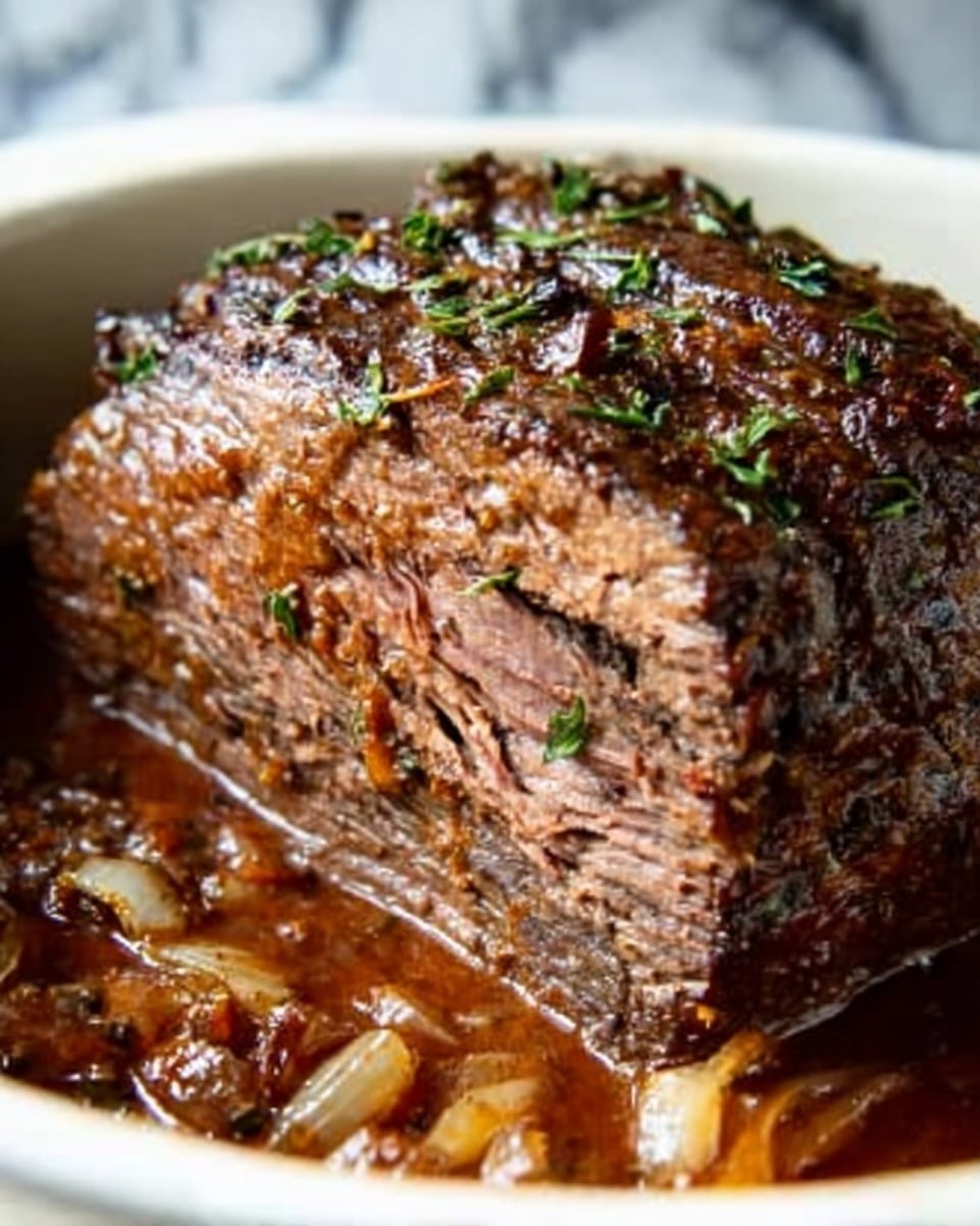 This image shows a thick cut of cooked beef roast in a white bowl, sitting in rich brown gravy with pieces of cooked onion around it. The top layer of the roast has a dark brown, crispy texture with small green herb sprigs on it. The sliced layers inside the beef are a mix of brown and pinkish shades, showing it is tender and juicy. The background has a white marbled texture. Photo taken with an iphone --ar 4:5 --v 7